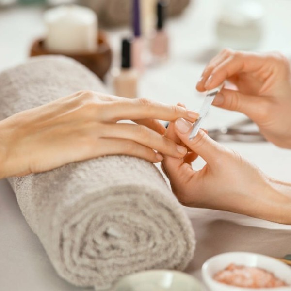 Close up shot of a woman in a nail salon receiving manicure by beautician with metal nail file. Woman getting nail manicure at spa centre. Beautician file nails to a customer in luxury salon.